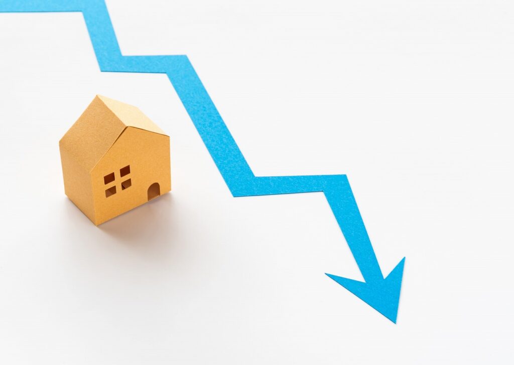 家の模型と資産が下落するイメージを示す右下がりの青い矢印