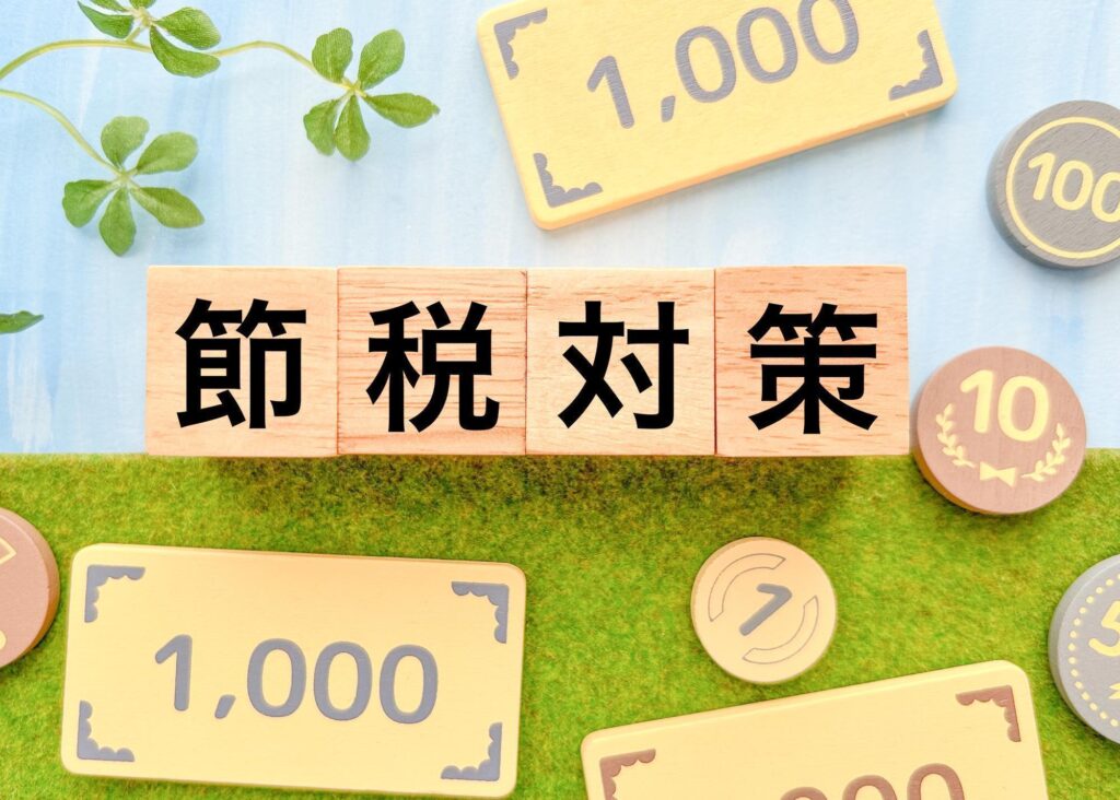 「節税対策」と書かれた木製ブロックと、周囲にお金を模したプレートやコインが配置されている