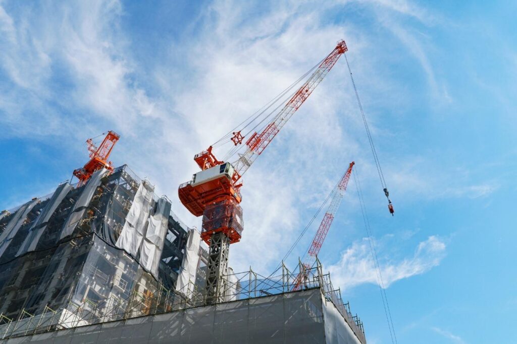 青空をバックにそびえ立つタワークレーンが設置された高層建築物の建設現場