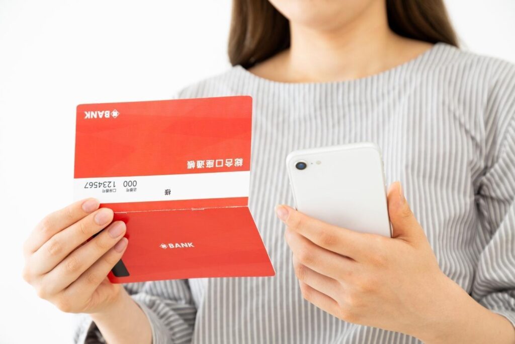 開いた預金通帳とスマートフォンを持つ女性