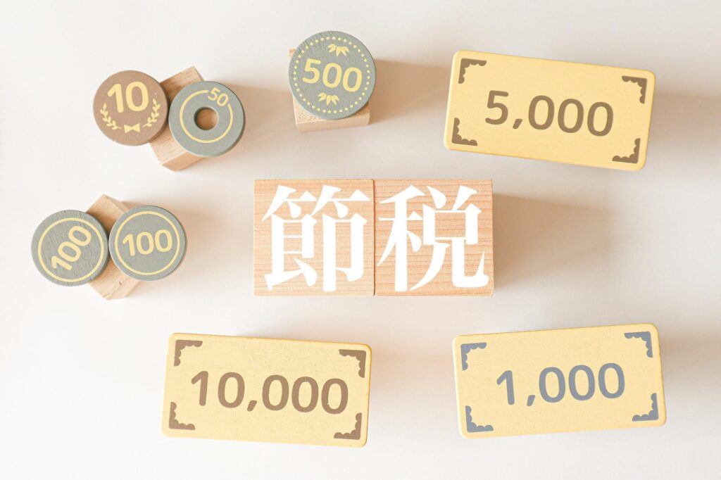 「節税」と書かれた木製ブロックと、紙幣・硬貨を模したパーツが並んだ、節税やお金の管理をイメージした構成