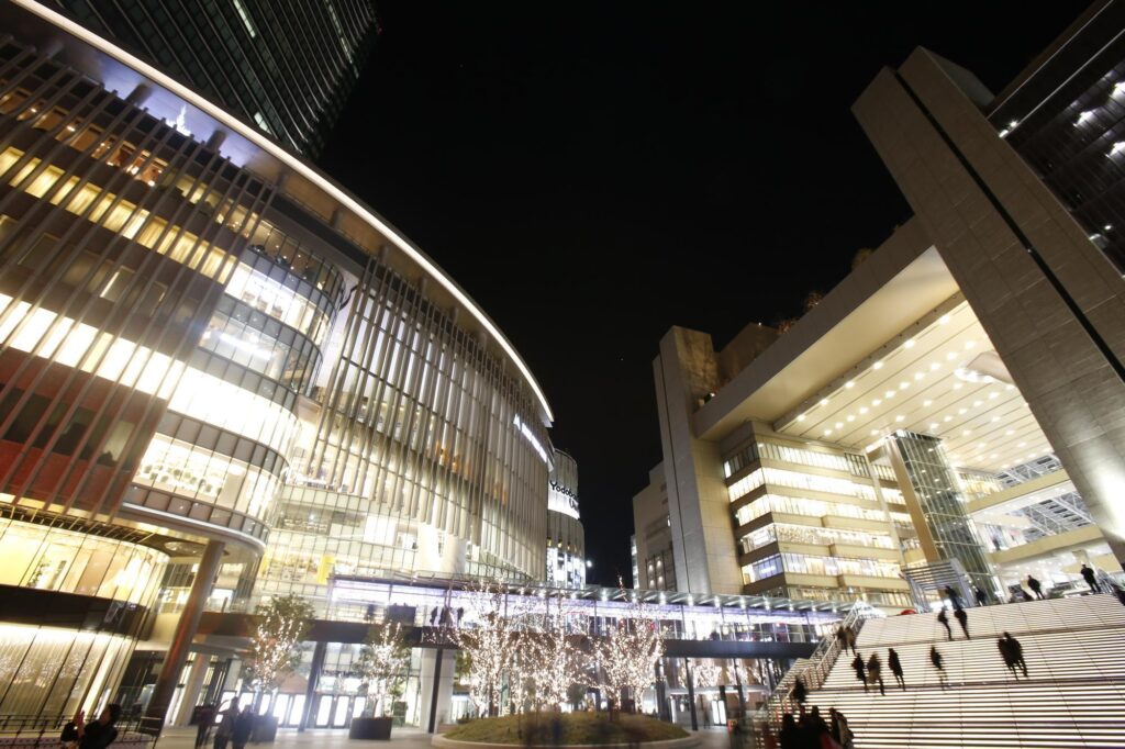 夜間にライトアップされた大型商業ビルと階段を行き交う人々の様子