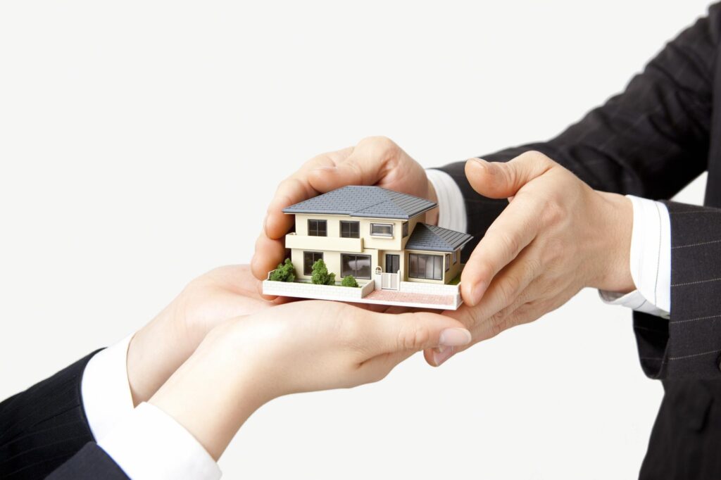 スーツを着た人物が両手で住宅模型を手渡している様子