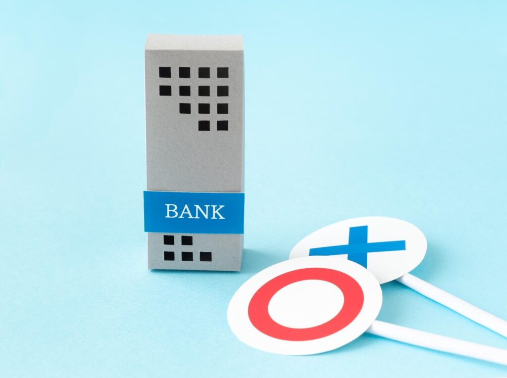 「BANK」と書かれたビルの模型の横に、◯と✕が描かれた札が置かれている