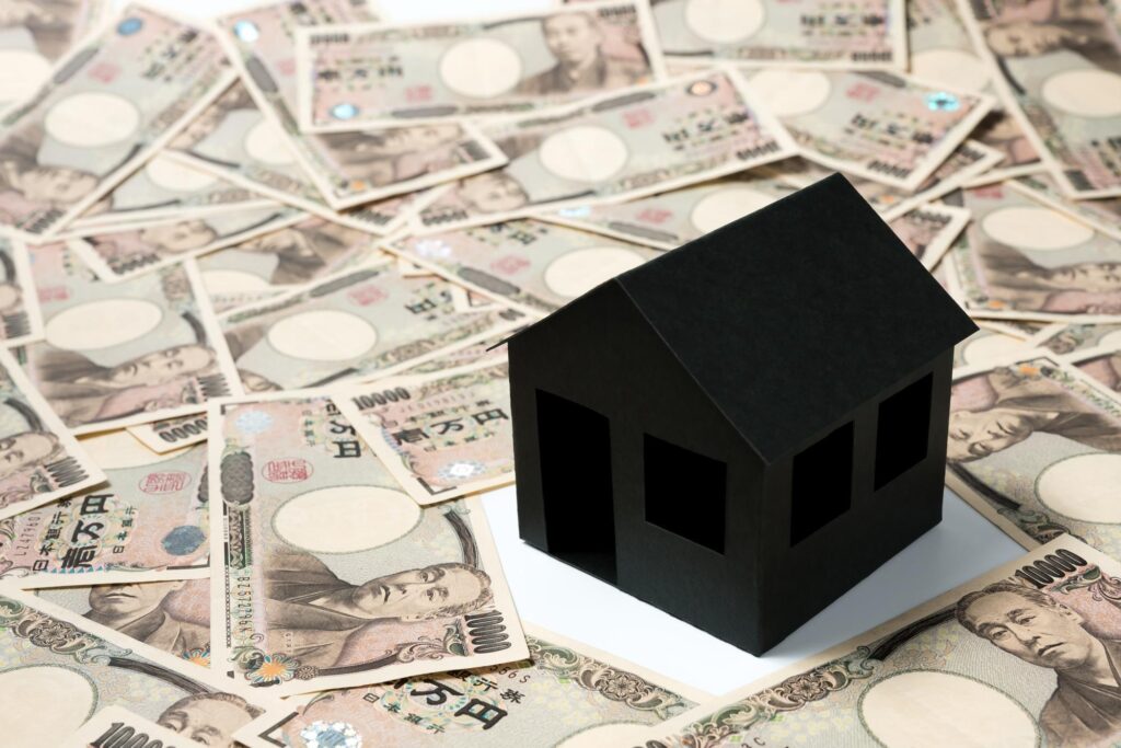 敷き詰められたたくさんの1万円札の上に黒い家の模型が置いてある
